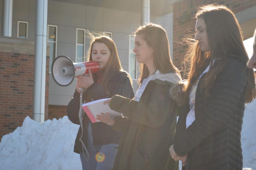 Senior Erica Lemcke and juniors Hannah Sween and Anna Weirz announce the names and ages of each victim of the Parkland shooting while other students light candles, one for each victim.