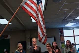 A group of students gather around the flag to recite the Pledge of Allegiance. Students recite the Pledge once a week. 