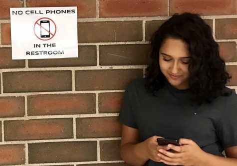 Junior Maleka Hussein stands in front of "no cell phones In the restroom" sign after exiting the ladies restroom. You can find these signs all around the school.