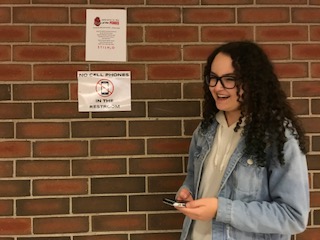 Junior Isabelle Rustad stands next the the No cell phones in the restroom sign, which are posted around the school.
