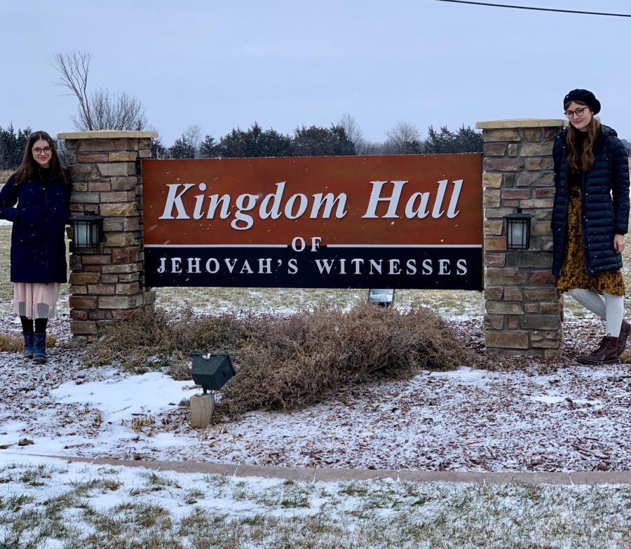 Sophmores Selah Clasen and Madison Grayden pose at a sign on Saturday December 29 just outside of the Kingdom Hall where their community comes together to share their faith.