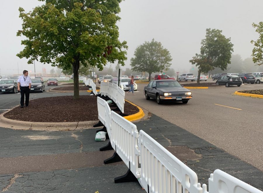 The students and staff have had to adjust heavily to the additions to the lot. Cars drive around the barriers and a student walks in the designated crosswalk as a security guard keeps watch over the new system.