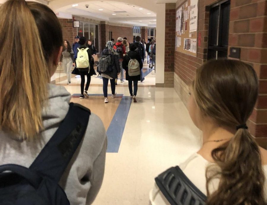 Juniors Kaehla Quinn and Eliza Darby walk through the halls. Eliza is wearing an Under Armor backpack while Kaehla is wearing a North Face backpack, both common brands students wear.