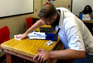 Math teacher Peter Hamilton takes precautions by wiping down desks. Hamilton ensures safety for students in the classroom.
