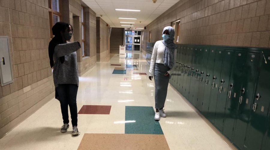 Link Leader Sadyia Farah showing freshman Safiyo Farah where to go for her class. They are keeping their distances apart from each other and wearing masks. 
