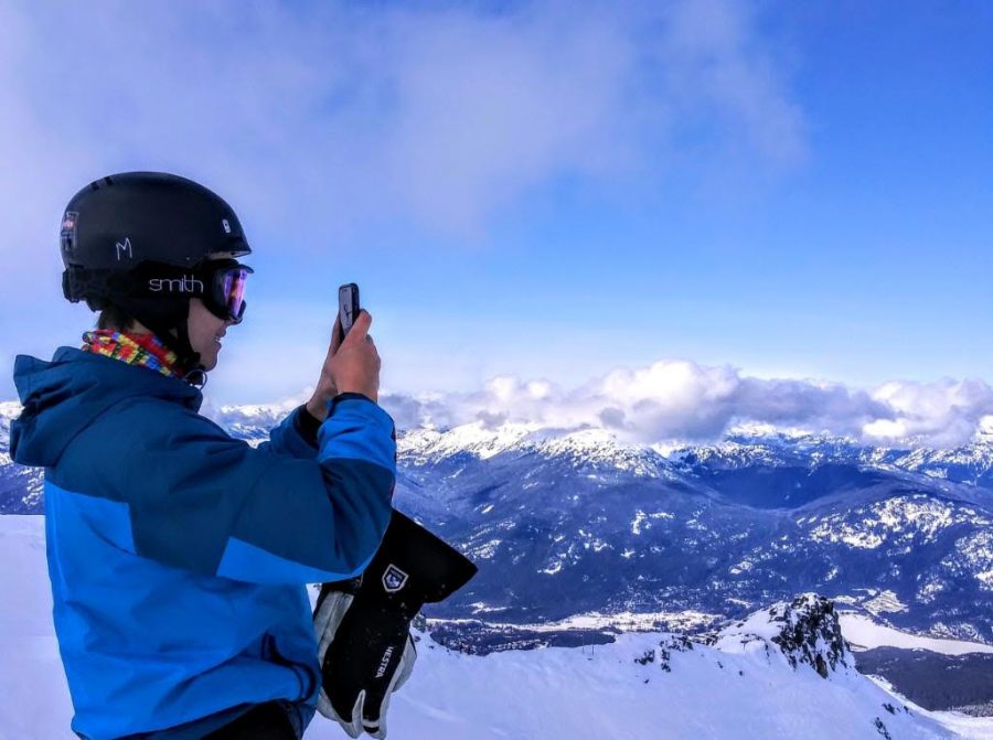 Junior Jacob Carlson stops skiing and takes a picture of the scenery while being photographed by his father.