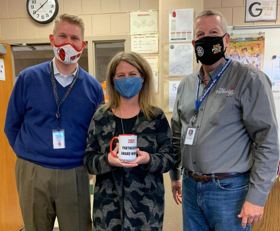 Math teacher Kathy Meyer stands beside principal Rob Bach and executive director Rick Robbins after being suprised with the news that she had been nominated and won a Partnership Award. Along with the recognition and honor bestowed upon her, she also receives an excellent mug.