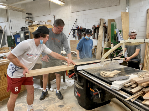 Senior Alex Corbett works with carpenter Marty Peterson, from Cates Fine Homes, and freshmen Carson Bahr and Grant Heinert on the river epoxy conference table in the school’s woodshop room.
