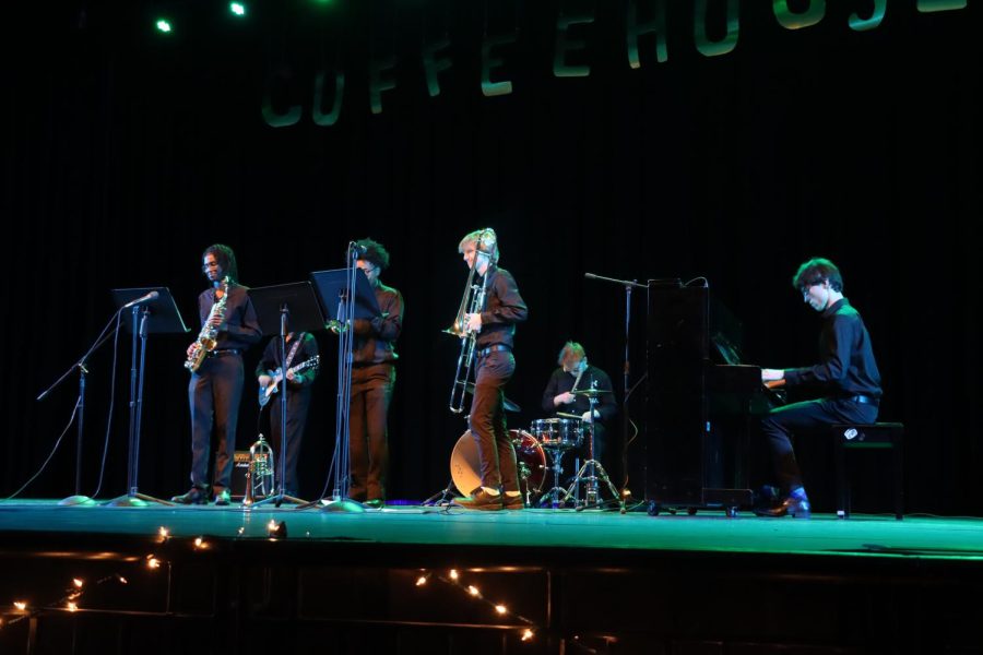 Band RNS plays I I want you back by the Jackson 5 at Coffee House. Seniors Kiran Kumaran, Joseph Casell, Caleb Cabede, Julian Schwendemen, Michael May and sophpomore Owen Cosgrove are pictured from right to left plaing the saxophone, electric guitar, trumpet, trombone, drum set and pianos respectively. The band plays on stage under a sign that reads coffeehouse .
