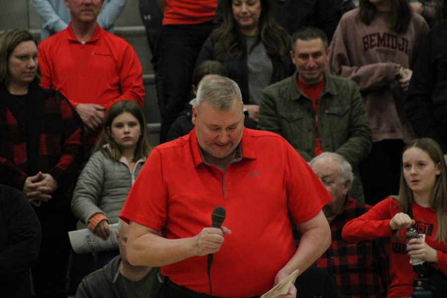 Chris Engler holds a microphone and share a few words at a basketball game.