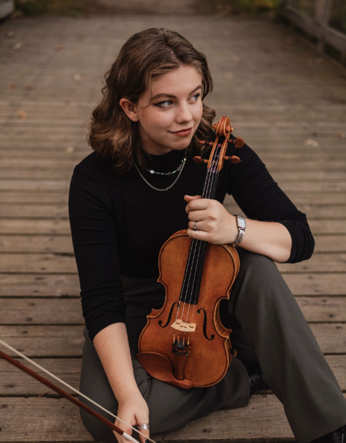 Grace Weitzel sitting on a boardwalk holding violin