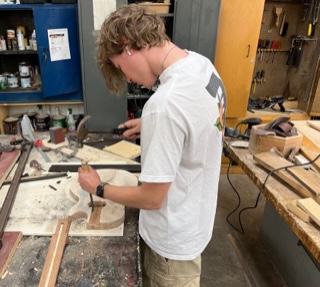 Student in the wood shop carving wood into the body of a guitar.