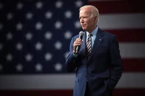President Joe Biden standing in front of an American flag, speaking into a microphone.