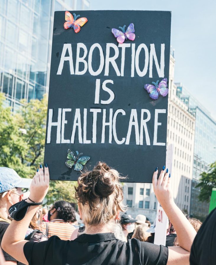 Someone holding a black sign that says abortion is healthcare in white letters