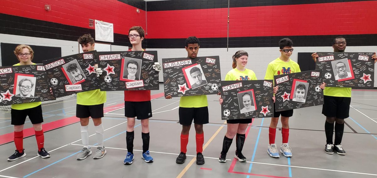 Seniors Jack Ridgeman, Mason Mora-Clark, Chase McCann, Mubarek Adem, Sophie Wynne, Sam Enright and Femi Alabi hold their posters after their final game of the soccer season.