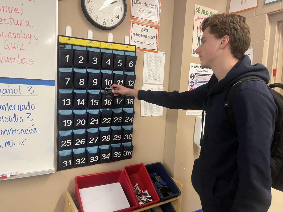 Sophomore Dustin Jurca puts his phone in the cell-phone caddy before class. The cell-phone caddy has been the high school's cellphone policy this year.