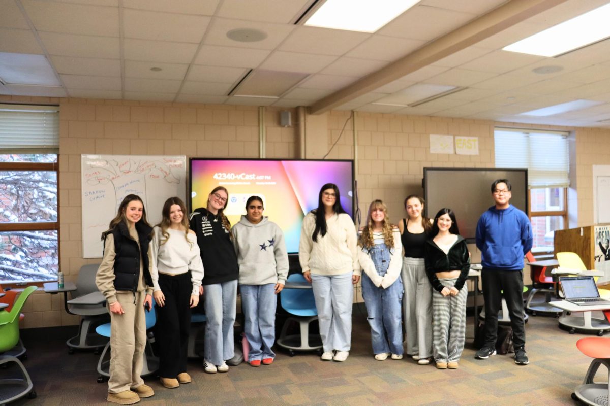 Students and speech team members, Ella Venzke, Riddih Singvi and Cecilia Wilson, among others, huddle together as a group photo is taken.
