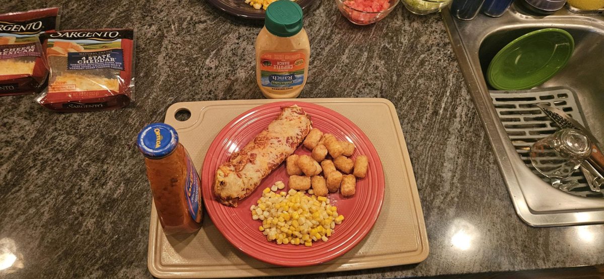 A completed home-cooked meal is displayed in a kitchen environment. The plate includes chicken with potatoes and corn.