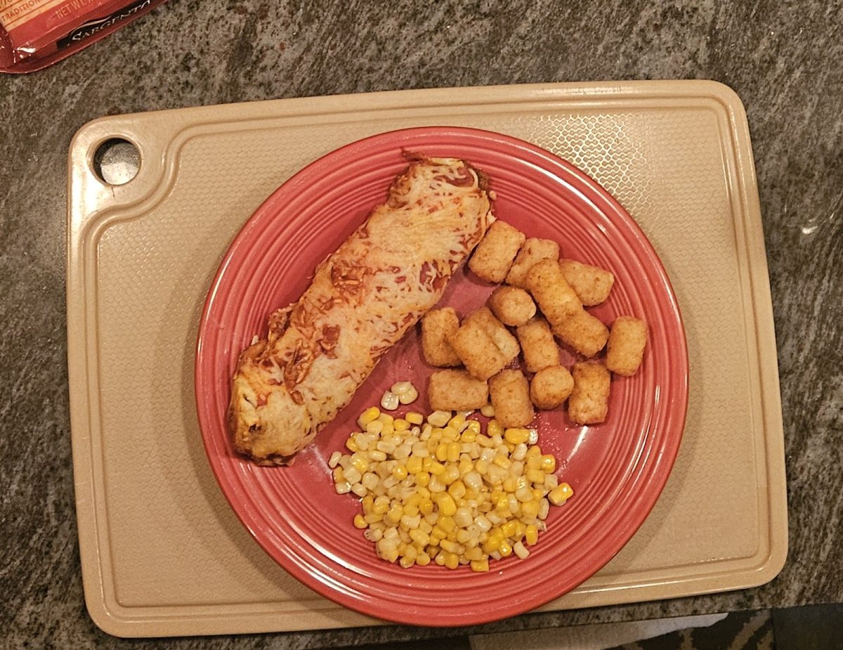 A home-cooked meal sits on a red plate with chicken, potatoes, and corn. The dinner was prepared and served in a kitchen setting.