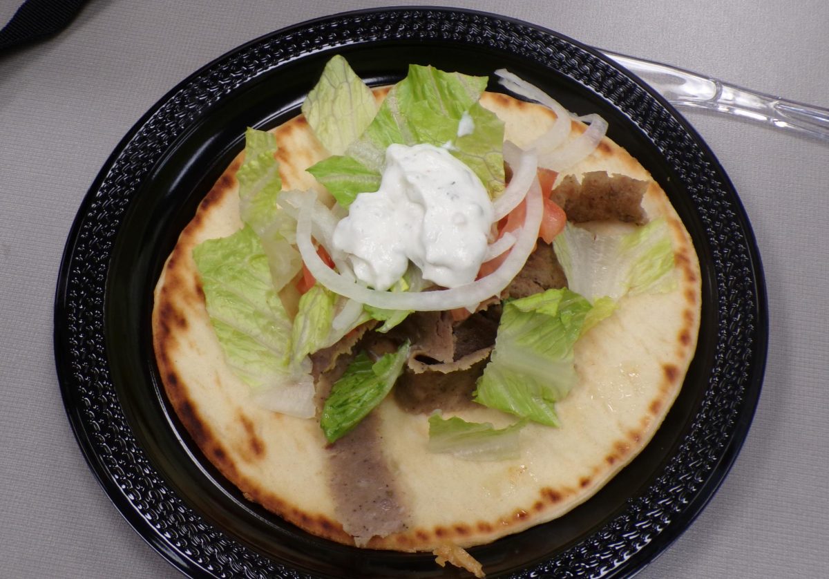 A circular black plastic plate frames the gyro and its large array of toppings. the mixture of crisp lettuce, lamb meat, and blob of tzatiki sauce contrast to the black plate.