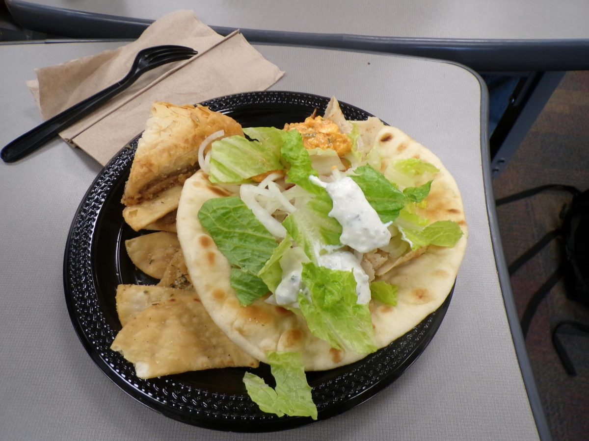 A chicken gyro sits on the plate with fresh lettuce and creamy sauce. Sweet baklava and soft pita pieces surround it.