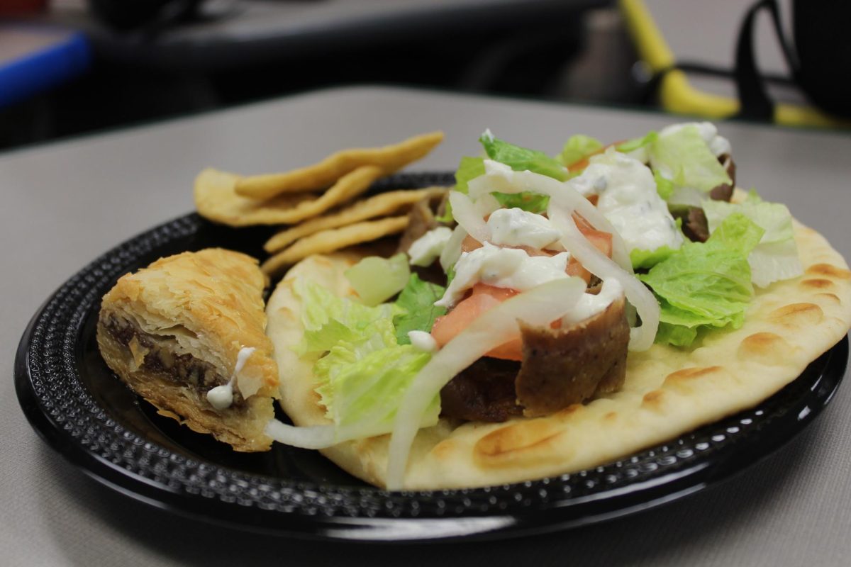 The black crowded plate sits atop of a gray desk. Atop the plate sits a well portioned gyro, not too much not too little