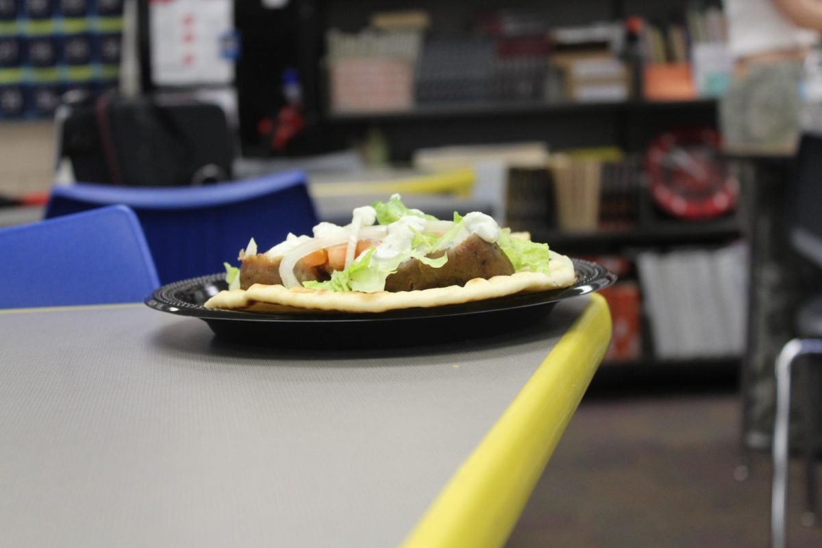 The plate distances itself from the camera, with a yellow line on the side of the desk from the plate to the camera. The plate still packed however the pita chips are gone, with the plate now being occupied by the gyro and baklava.