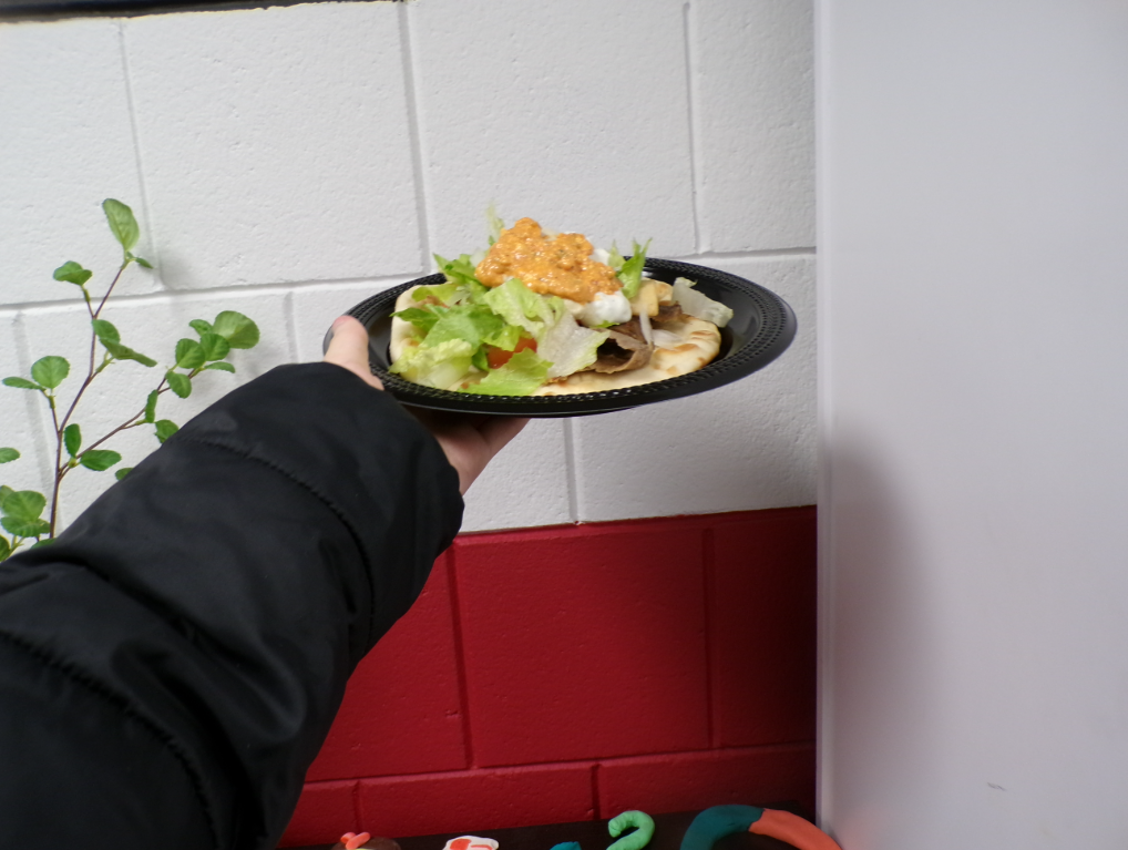 A freshly made gyro being held, showcasing the layers of each ingredient. Each component adding their own unique element to the dish.