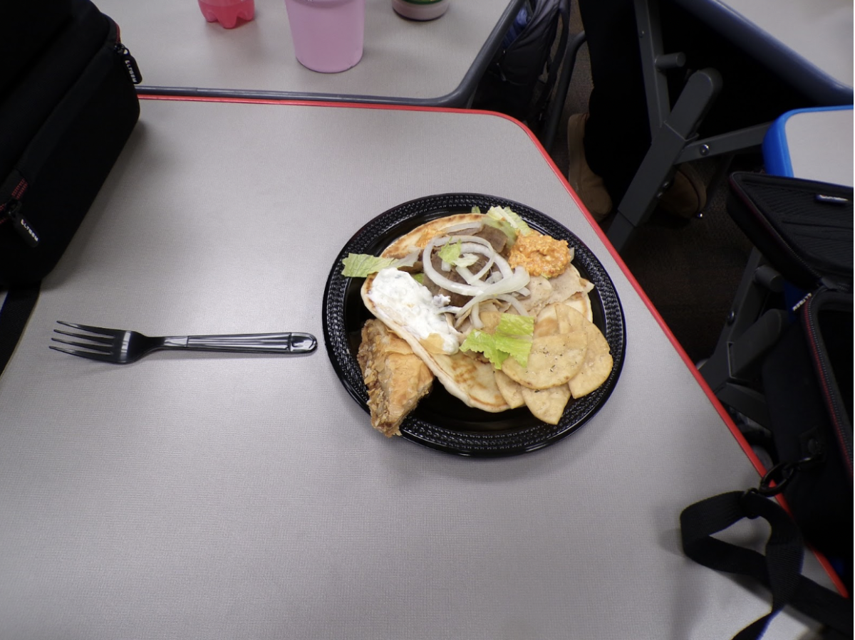 The fork pointing to the dish with a higher perspective of the gyro itself. The onions, lettuce and sauces, combining well with each other. 