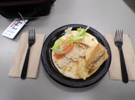 A strategically created gyro with lettuce and tomato added into the savory style meal. The plate is framed by two forks and napkins to demonstrate the balance of Dinos Gyros.