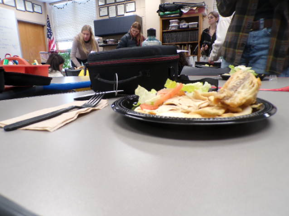 Flakey baklava and structured gyro on a black plate. The meal placed beside a fork ready for tasting.