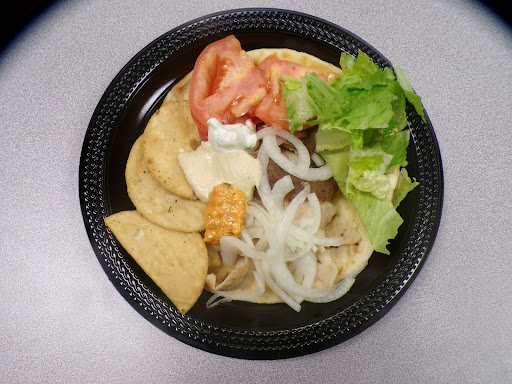 The plate of Greek food is seen on a light neutral colored table. The colors from the food on the plate, contrast sharply from the background.