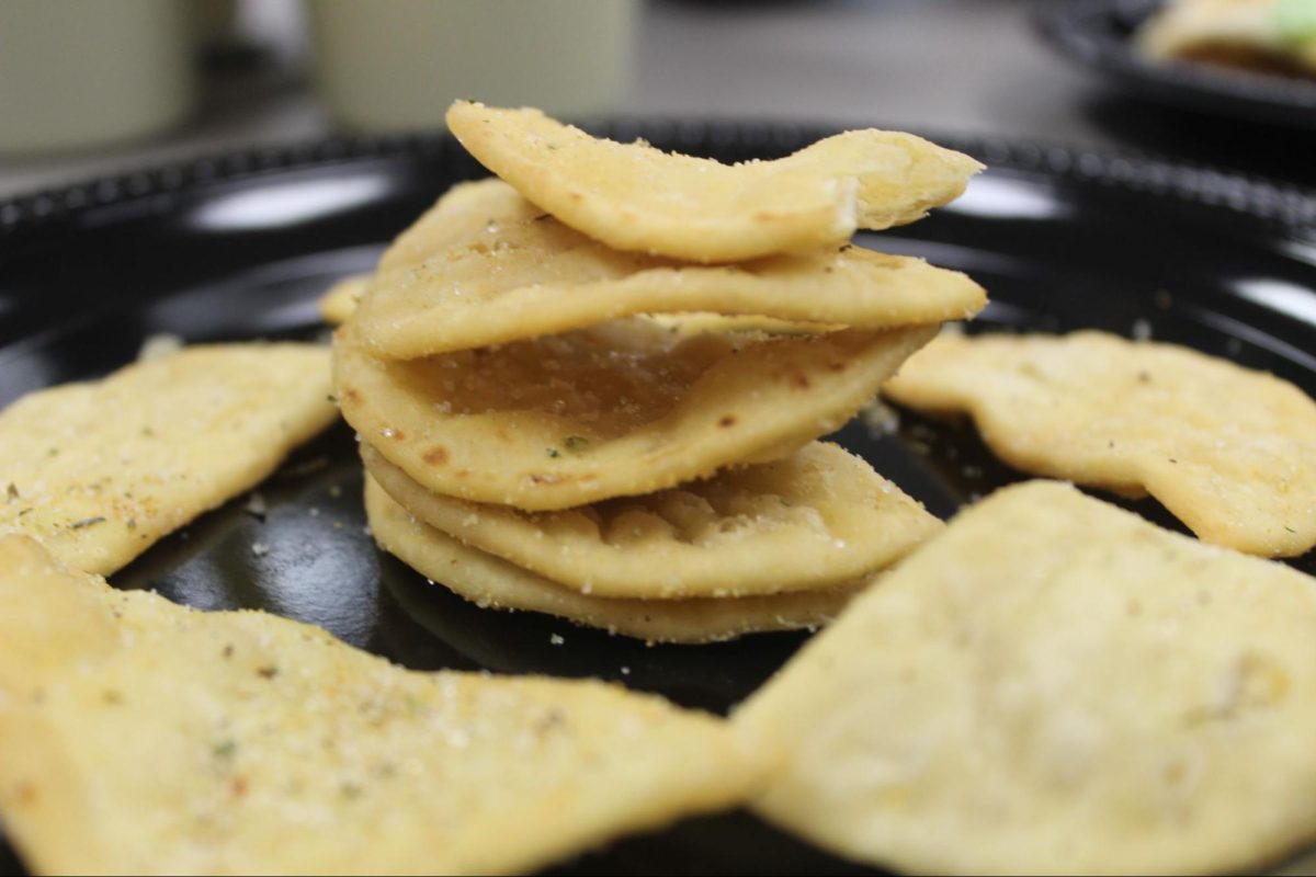 The stacked pita chips show a deep golden color with visible seasoning. The rough edges and small crumbs highlight the crunchy and crisp texture.  